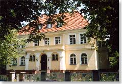 Ein Haus aus dem 19 Jhd., gelb angestrichen, umrahmt von Bäumen.